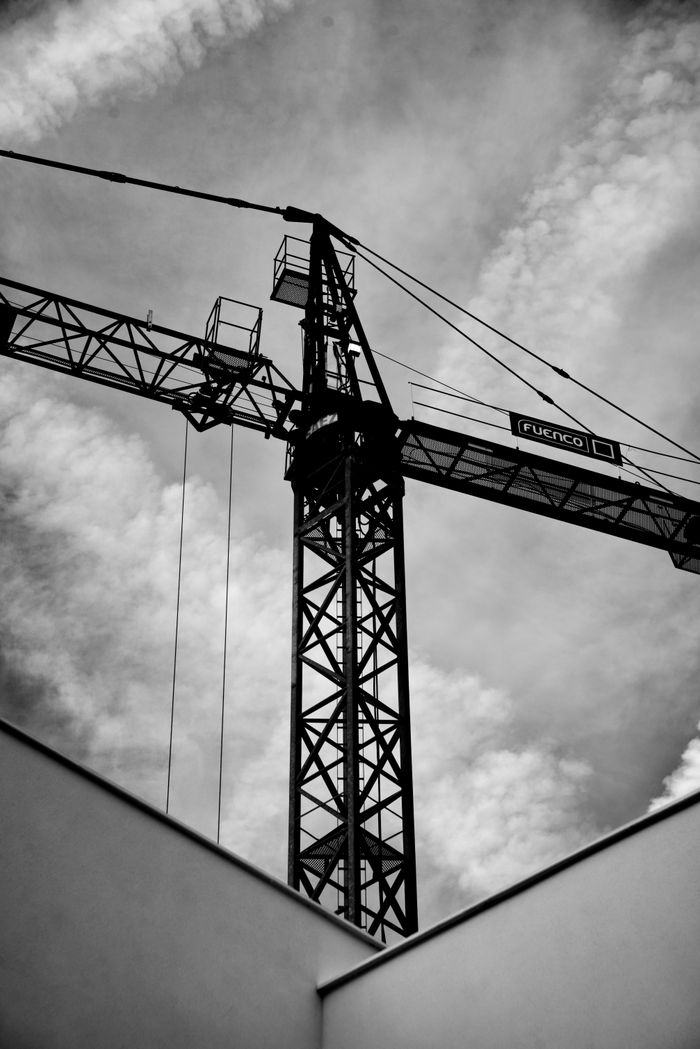 A striking black and white photo of a crane against a cloudy sky, exhibiting industrial elegance.