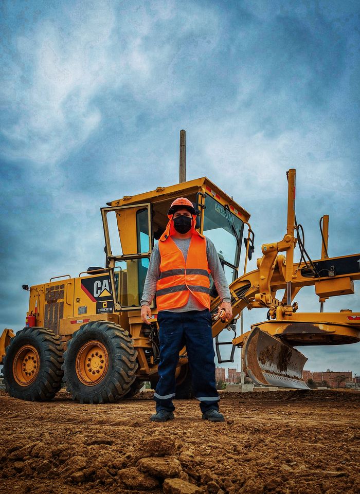 pexels photo 8809473 A construction worker in safety gear stands in front of a bulldozer under a cloudy sky on a worksite.